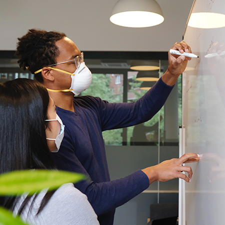 coworkers planning on a whiteboard while wearing masks
