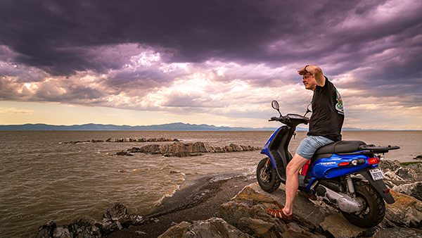 A man on a scooter looks out over a cliff to the ocean