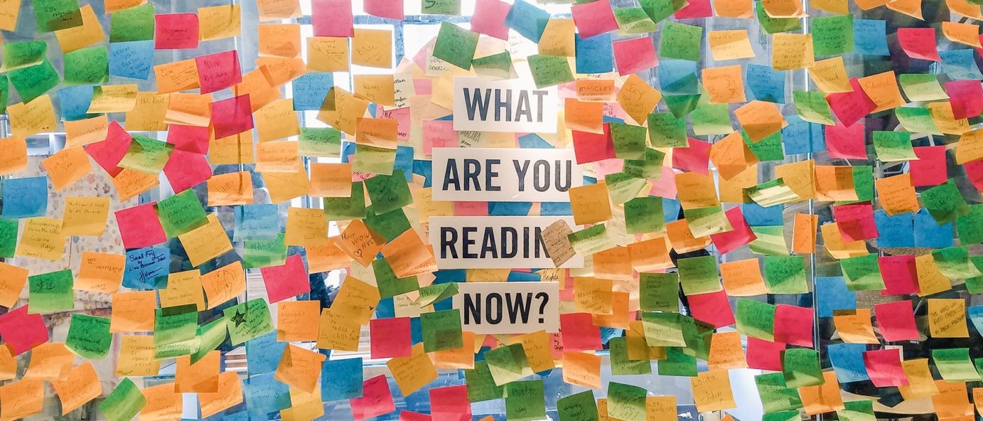 a window covered in sticky notes of different colors. In the center a sign that says "what are you reading now?"