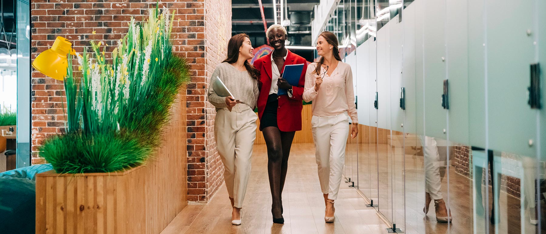 Three smiling women walk down an office hallway smiling at each other