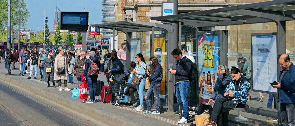 A large crowd waits at a streetcar stop.